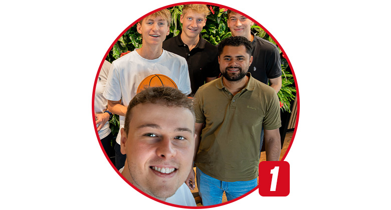 A young man takes a selfie with four others in front of a green plant wall, one is holding a basketball.