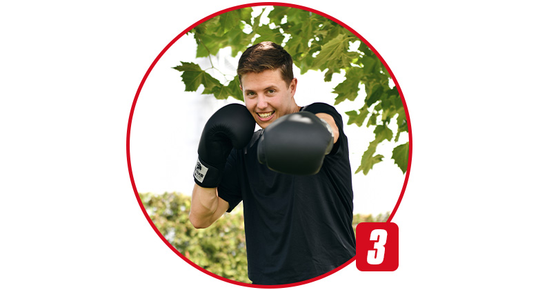 A young man wearing black boxing gloves stands in a fighting stance outdoors.