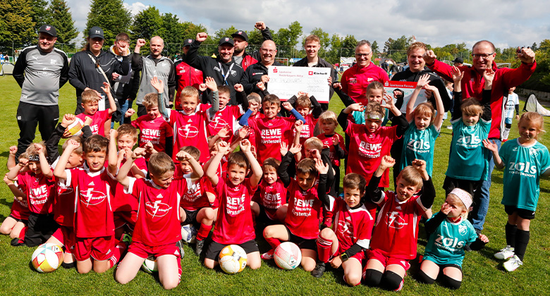 A large group of children in football jerseys cheers with their coaches on a football field.