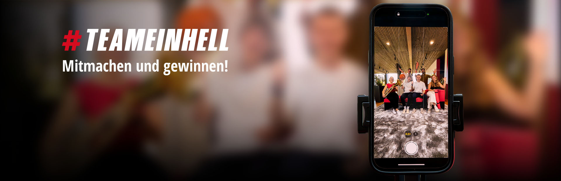 Auf einem Smartphone ist ein Gruppenfoto von sechs Personen mit Sportgeräten und Instrumenten zu sehen. Links steht: "#TEAMEINHELL Mitmachen und gewinnen!"