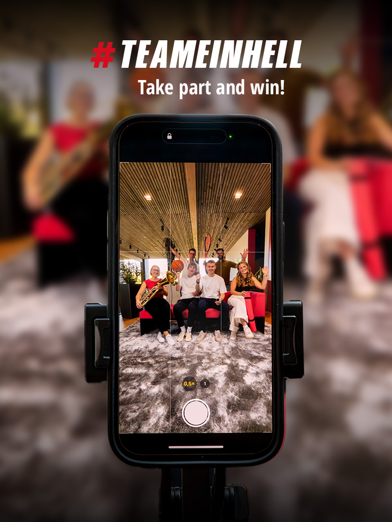 A smartphone shows a group photo of six people with sports equipment and instruments. Text above: "#TEAMEINHELL Take part and win!"
