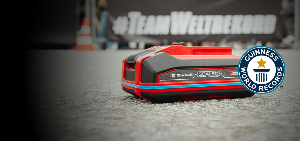 Einhell SEALED Akku Power X-Change 4,0 Ah liegt auf Asphalt, rechts das Guinness World Records „Record Holder“-Logo.