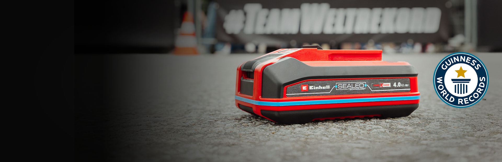 Einhell SEALED Akku Power X-Change 4,0 Ah liegt auf Asphalt, rechts das Guinness World Records „Record Holder“-Logo.
