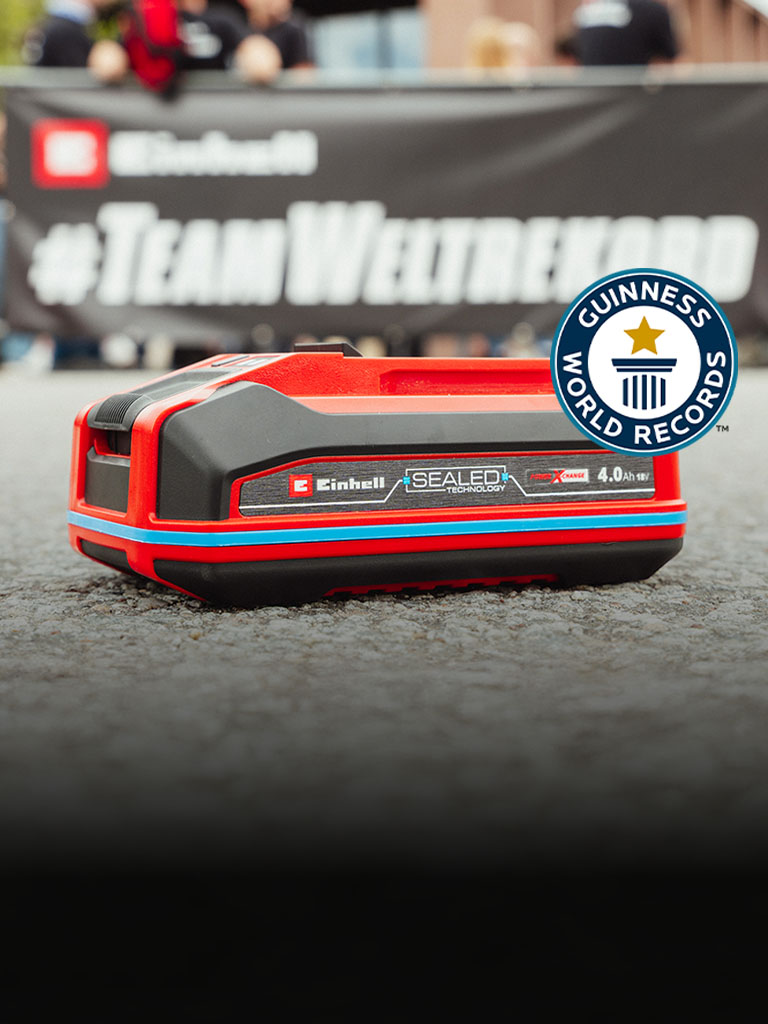 Einhell SEALED Akku Power X-Change 4,0 Ah liegt auf Asphalt, rechts das Guinness World Records „Record Holder“-Logo.